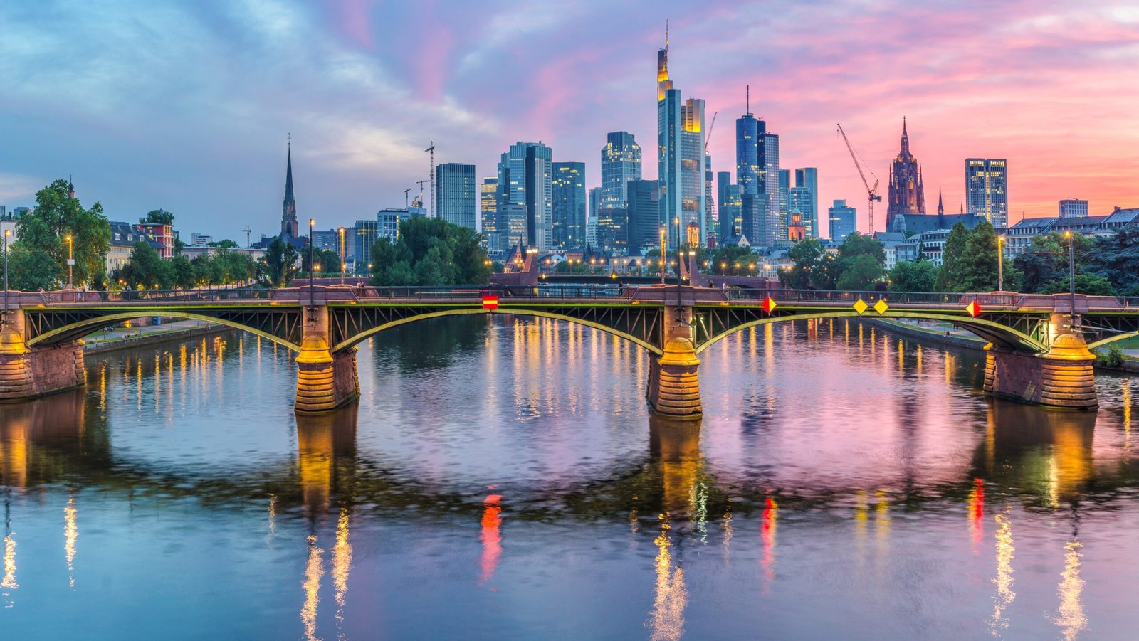 Skyline of Frankfurt at sunset with illuminated bridge over the river