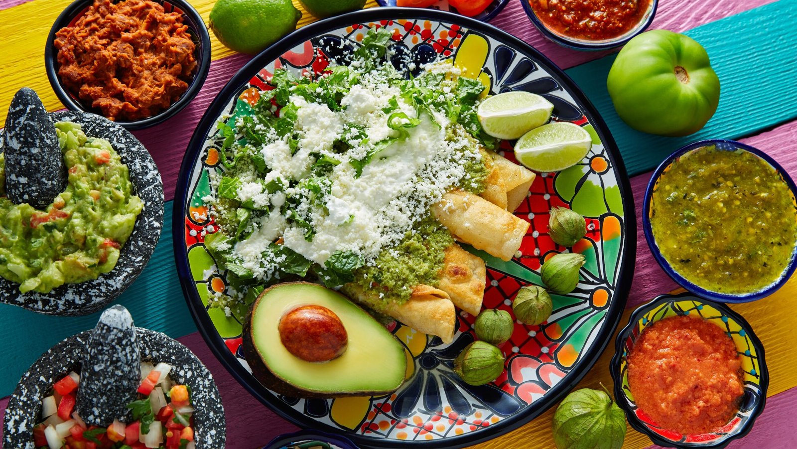 Mexican Green enchiladas with guacamole and sauces on a colorful table